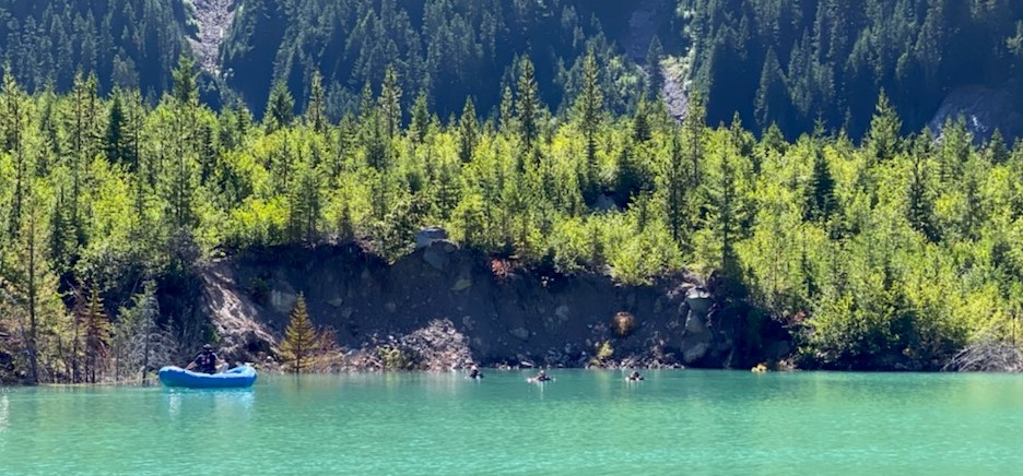 A dive team works out of an inflatable boat on a lake surrounded by trees.