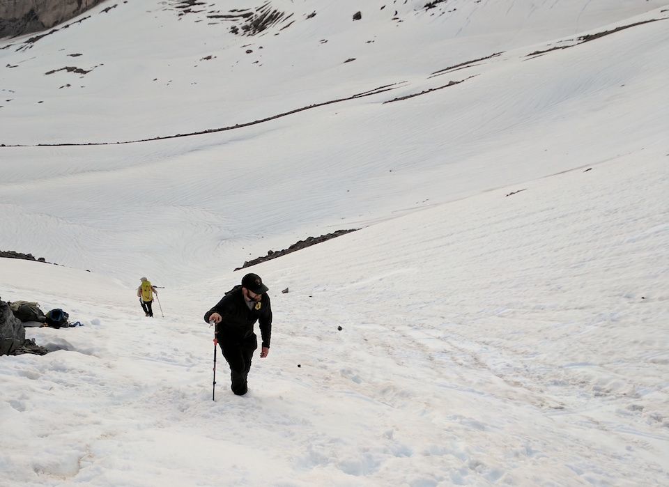 Ground search for missing skier A man hikes up a steep snow covered slope.