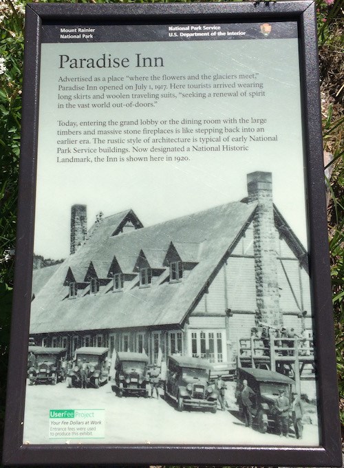 A small vertically-oriented wayside featuring a historic photo of a large wood building.