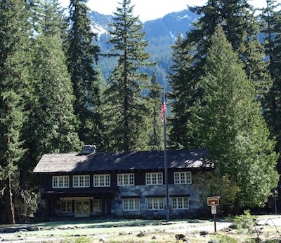 A rustic building built with rocks and timber framed by tall trees.