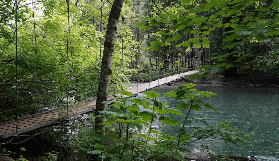 A narrow suspension bridge crosses over a clear blue river.