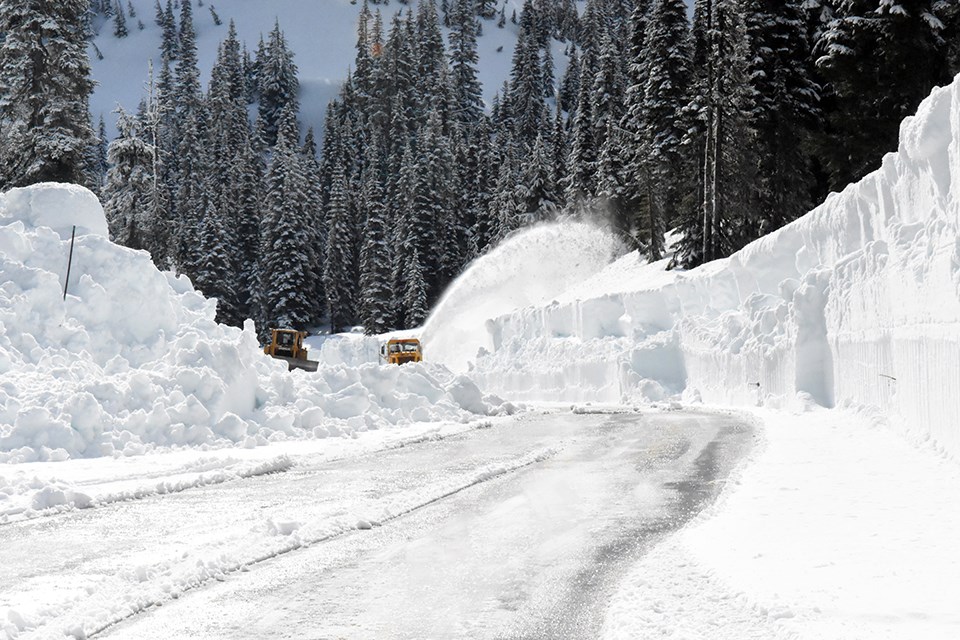 Two plows remove snow on partially covered road.