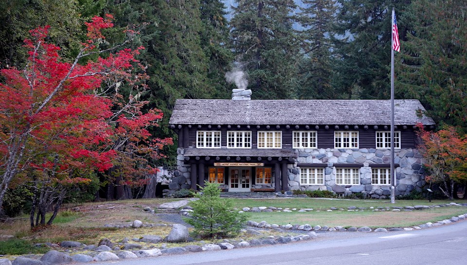 A two-story wood and stone building surrounded by forest and red vine maple trees.