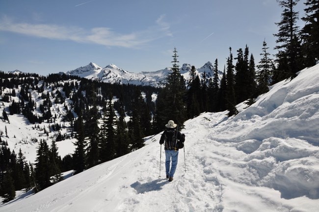 A hiker walks along a snowy trail in the mountains.