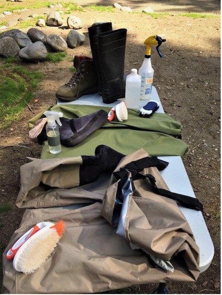 Clean waders and boots drying on a table next to brushes and spray bottles.