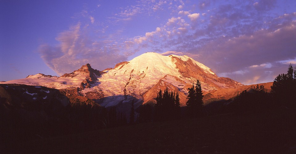 A glacier-covered mountain glows pink and red during sunrise.