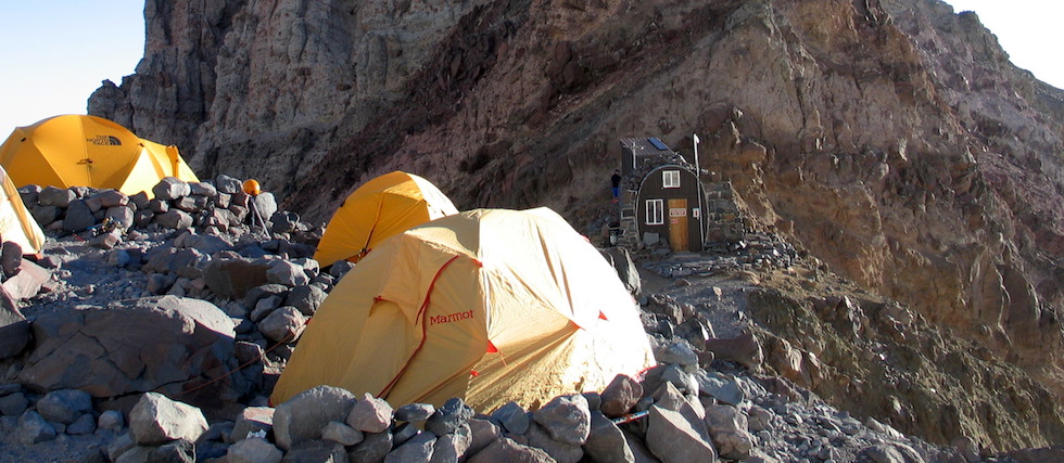 Tents and the stone house of Camp Schurman perch on a rocky ridge on the side of Mount Rainier. Tents and the stone house of Camp Schurman perch on a rocky ridge on the side of Mount Rainier.