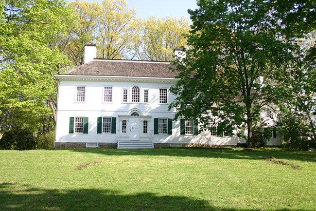 A large white Georgian mansion surrounded by trees and green grass