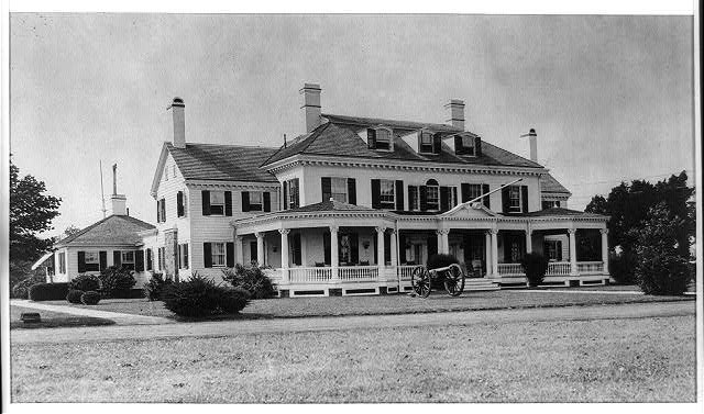 A black and white image of a large Georgian mansion with several modern additions such as porches and extra wings