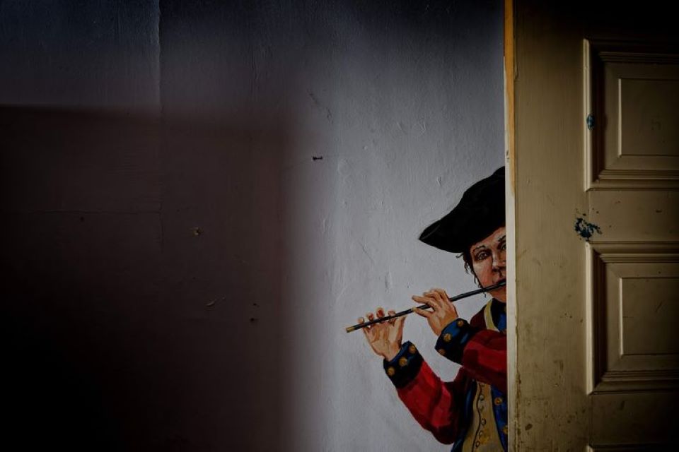 Wall painting of a young boy peering behind an actual open door, playing a fife and dressed as a Continental Army musician.