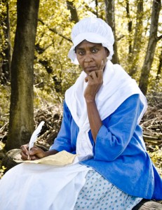 Theater actress Dr. Daisy Century in a blue an white 18th century costume, portraying the first published enslaved African American, Phillis Wheatley.