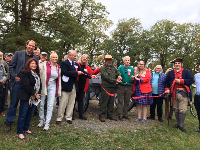 A group of people stading in front of a cannon while a ribbon is being cut