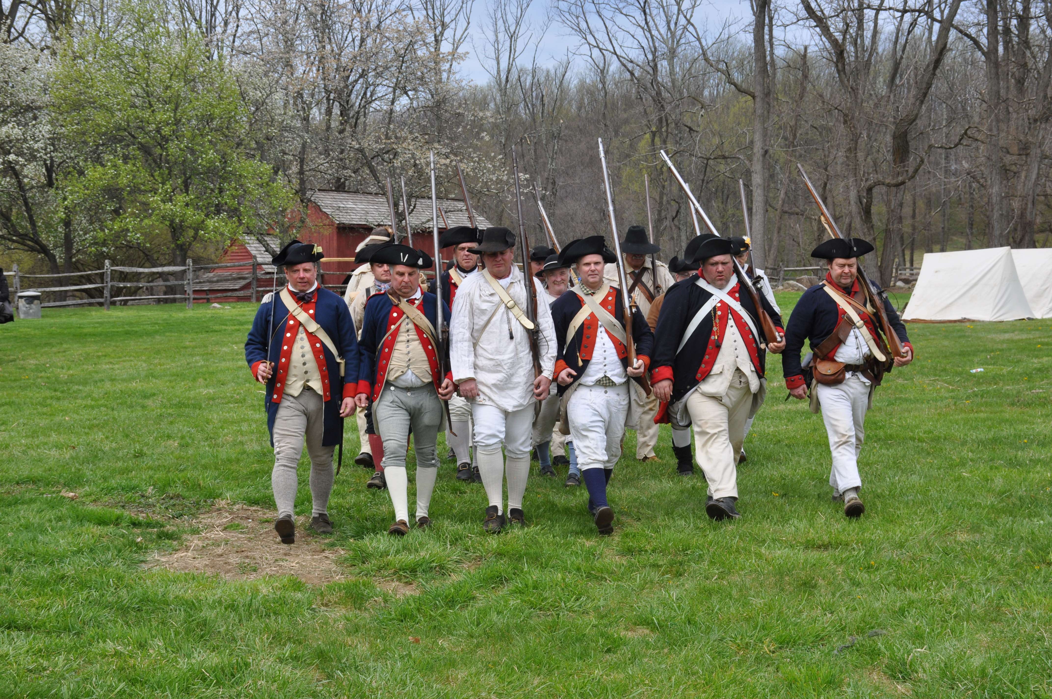 Soldiers practicing marching drills during annual spring encampment. 3 rows of 7 soldiers each, dressed in 18th century uniforms practicing marching drills.