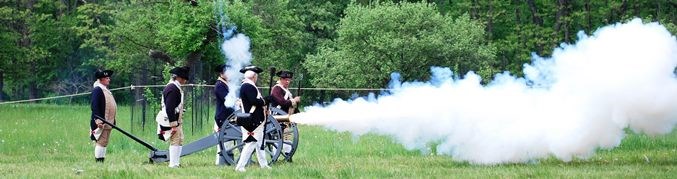A cannon is fired by 5 men dressed as Continental soldiers, with a billow of smoke coming from the mouth of the cannon.