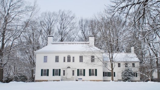 Washington's 1779-1780 Headquarters in winter.  A large white house with a center door surrounded by several trees and snow.