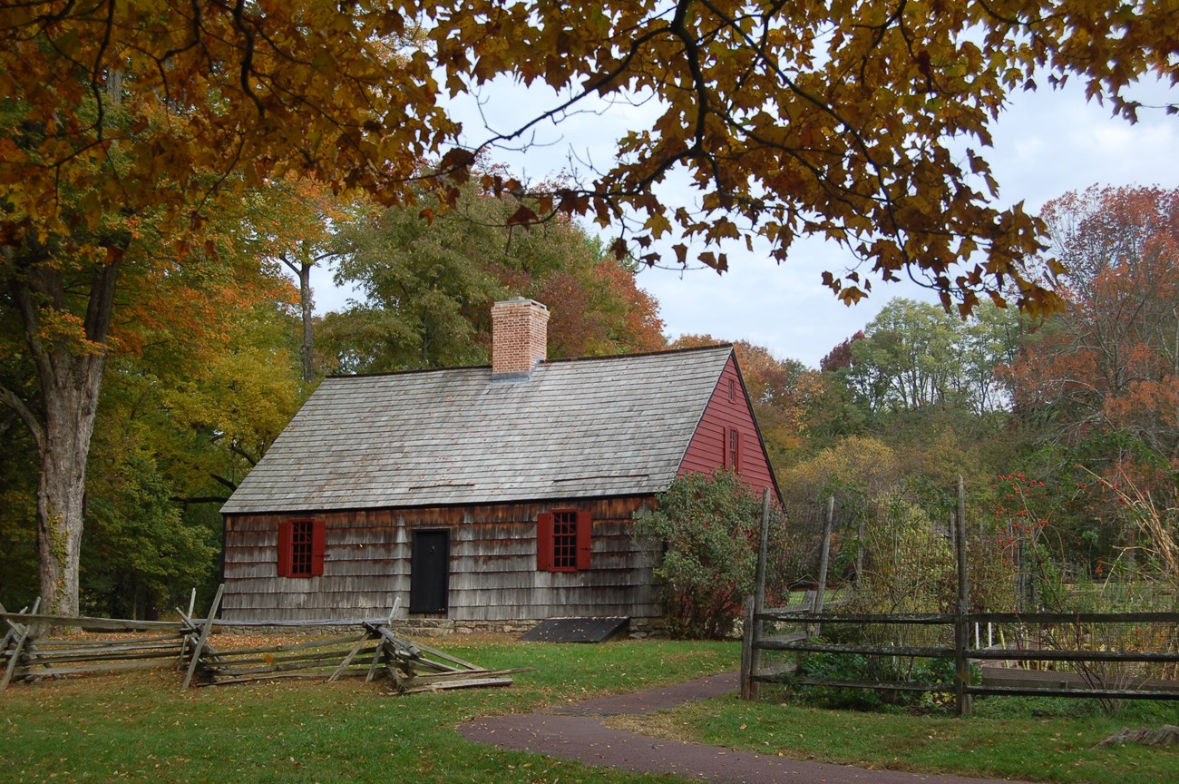 A historic two story farm house in the Cape Cod style with red siding, pine shingles, and a single chimney.