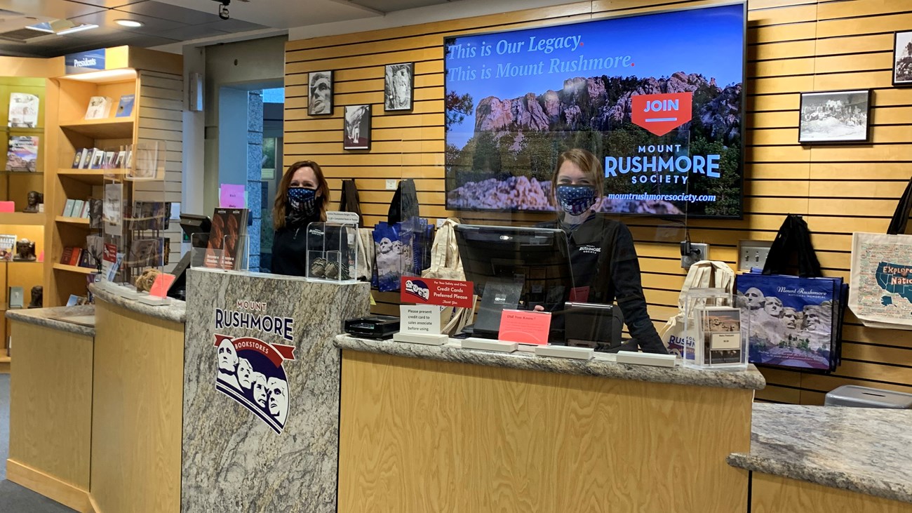 Two Mount Rushmore Bookstores staff members wearing face masks standing behind a check out counter.