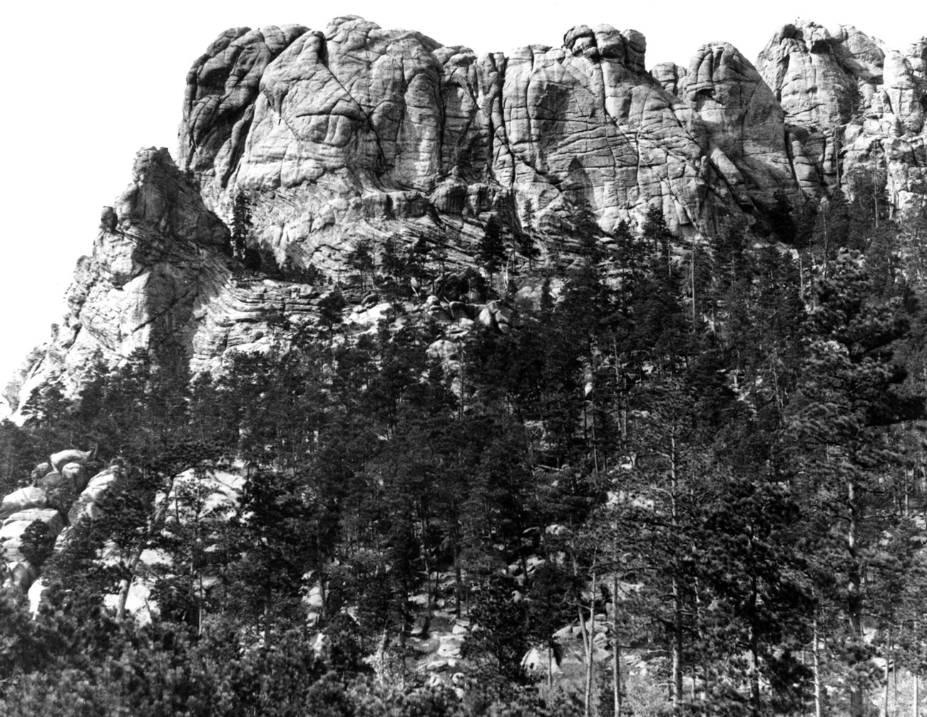 Black and white photo of Mount Rushmore before carving, with its wrinkled and weathered appearance as Charles Rushmore would have seen it in 1884-85.