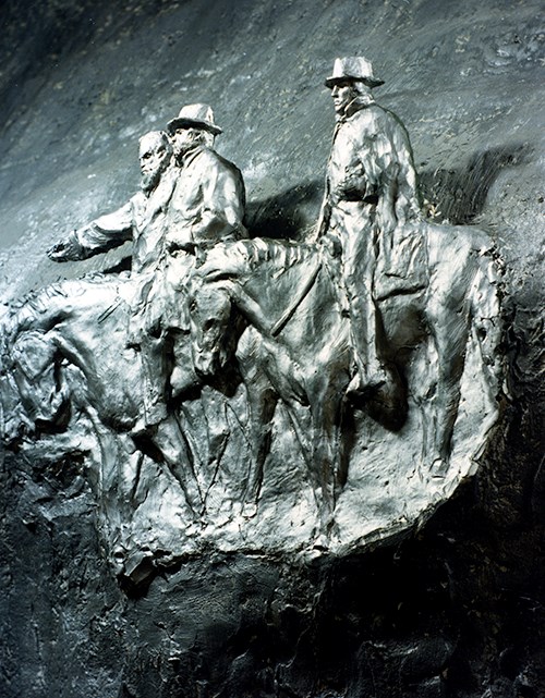 A scale model for the Stone Mountain carving portraying three men on horses, all wearing long overcoats and the two nearest wearing hats.  The horses and men all face towards the left