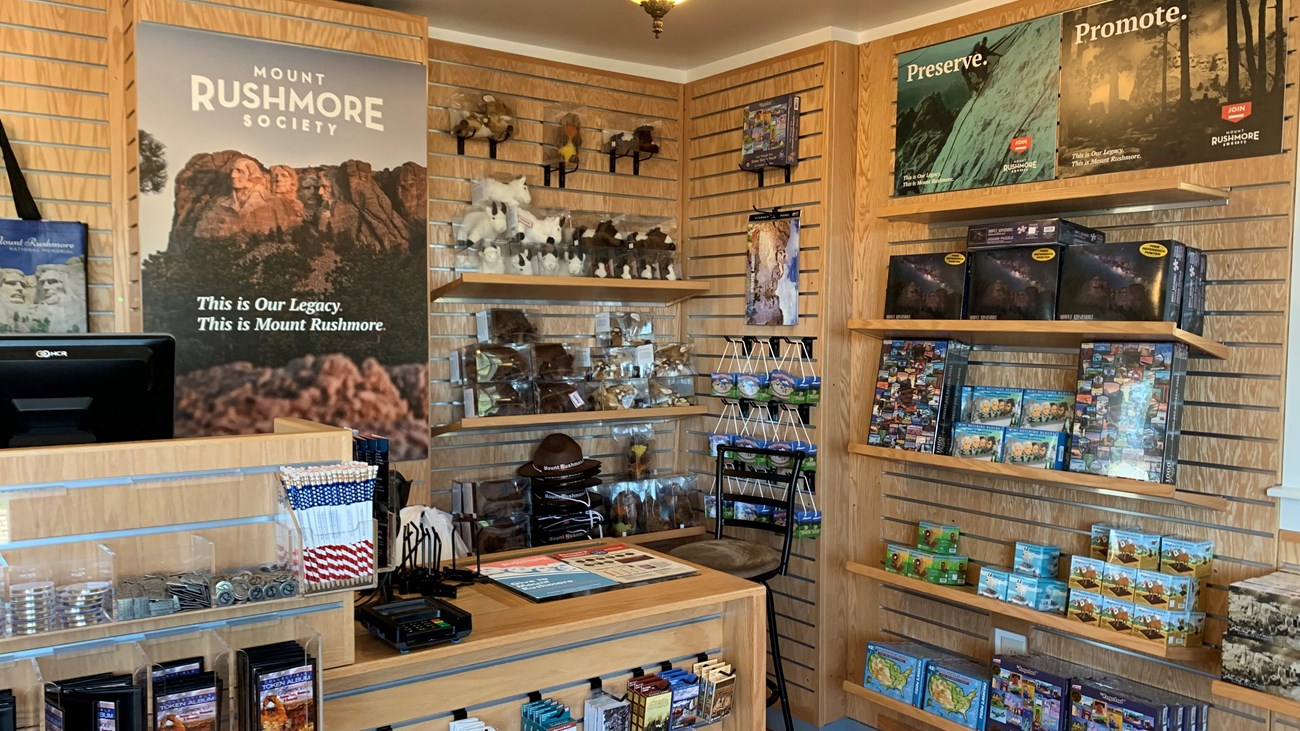 Store counter with cash register in front of a brown wall with shelves filled with bookstore merchandise.