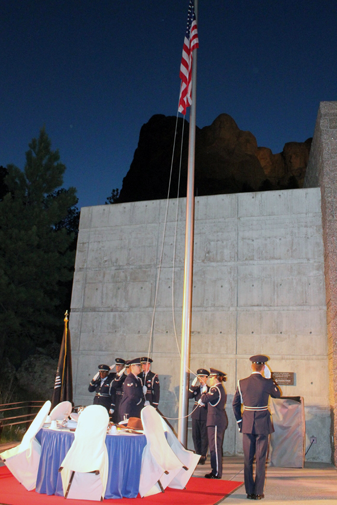 Members of a United States Air Force color guard retreat the flag as Mount Rushmore is illuminated.
