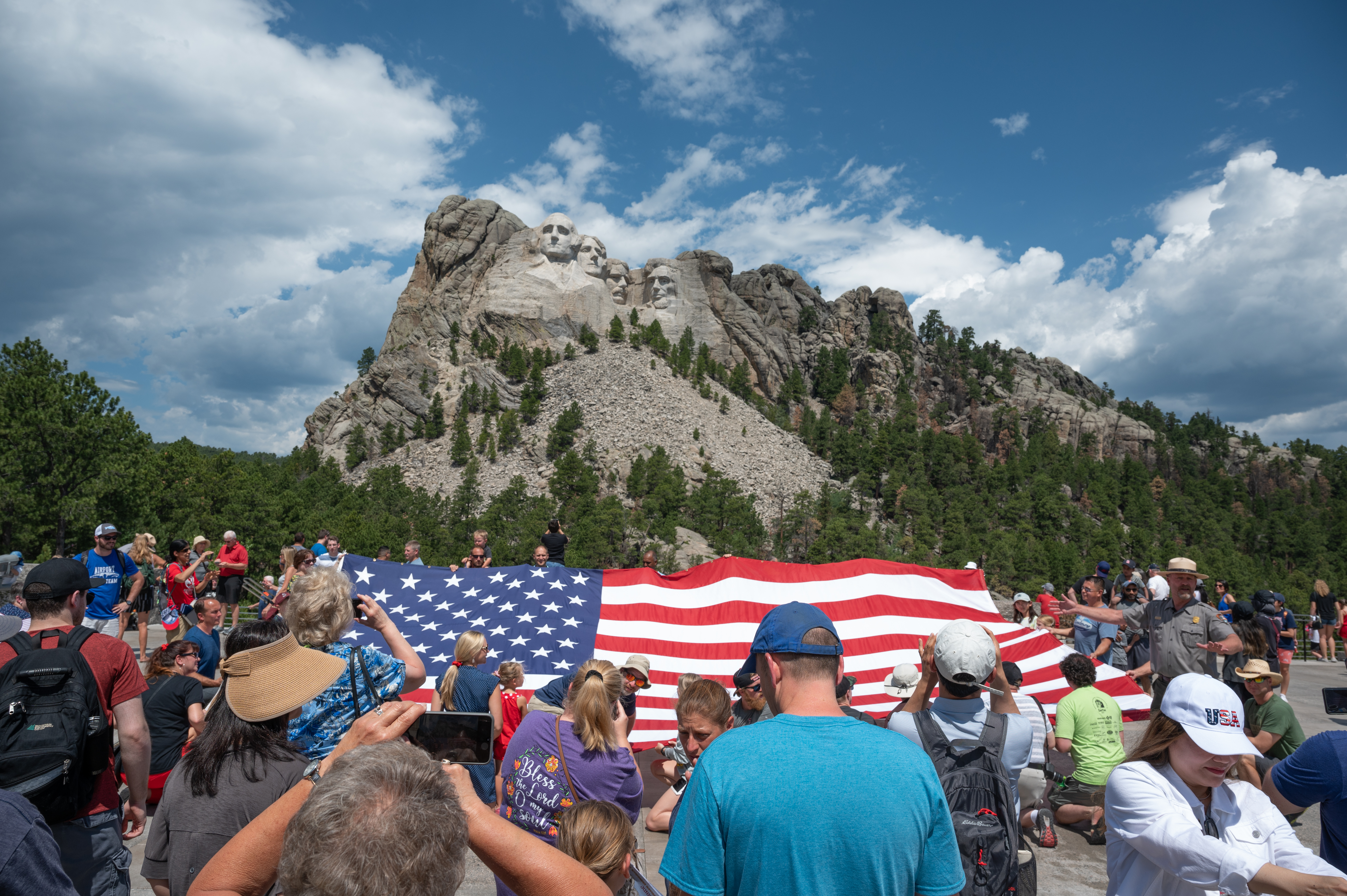 _DSC0534 Crowd of people standing with a large American flag in front of Mount Rushmore.