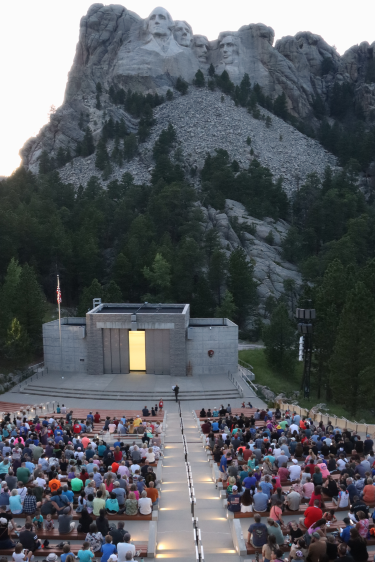 Visitors in the amphitheater for the evening program, with Mount Rushmore in the background.