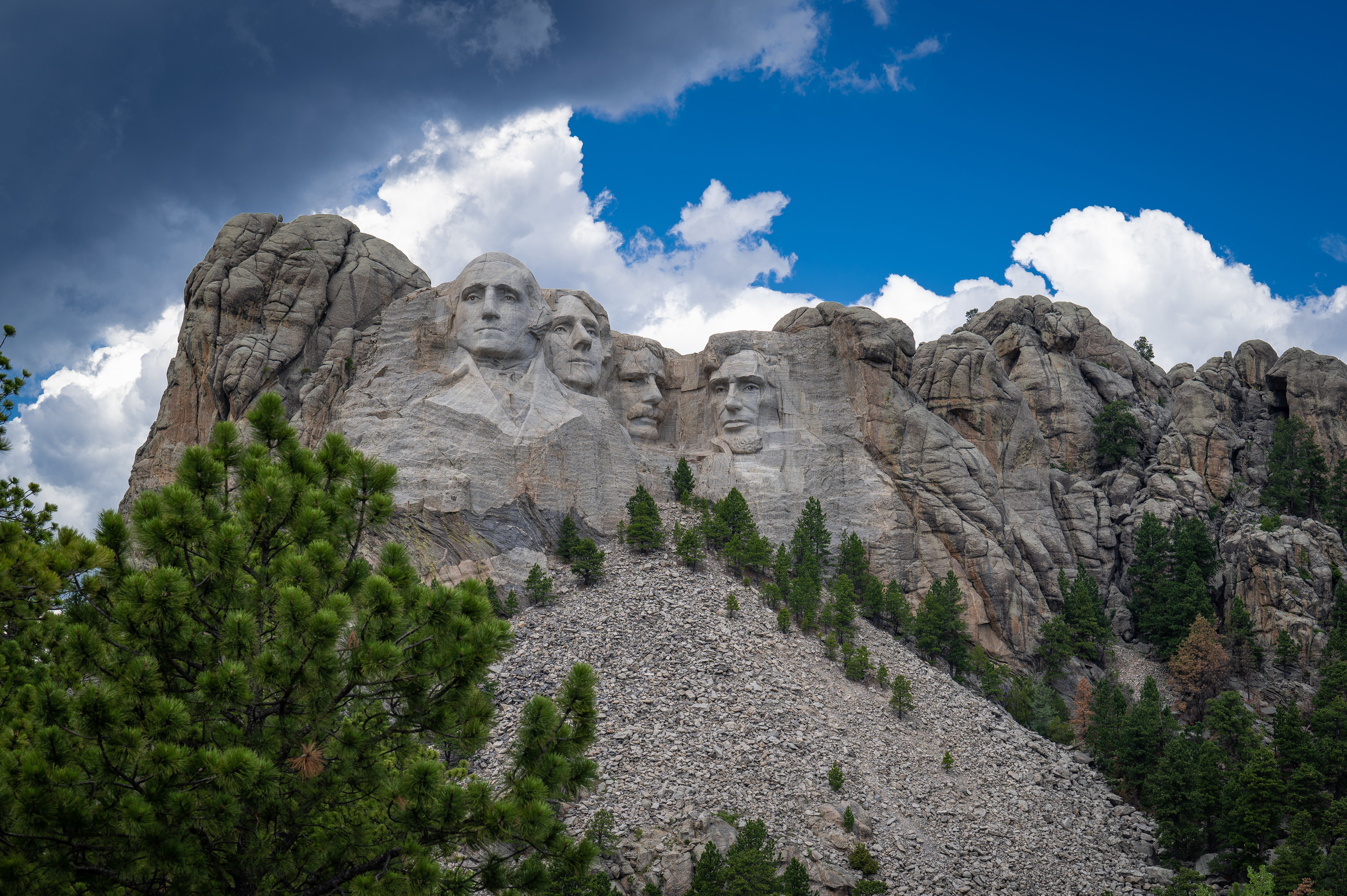 heads and faces of four men carved into a granite mountain underneath a blue sky and thunderclouds.