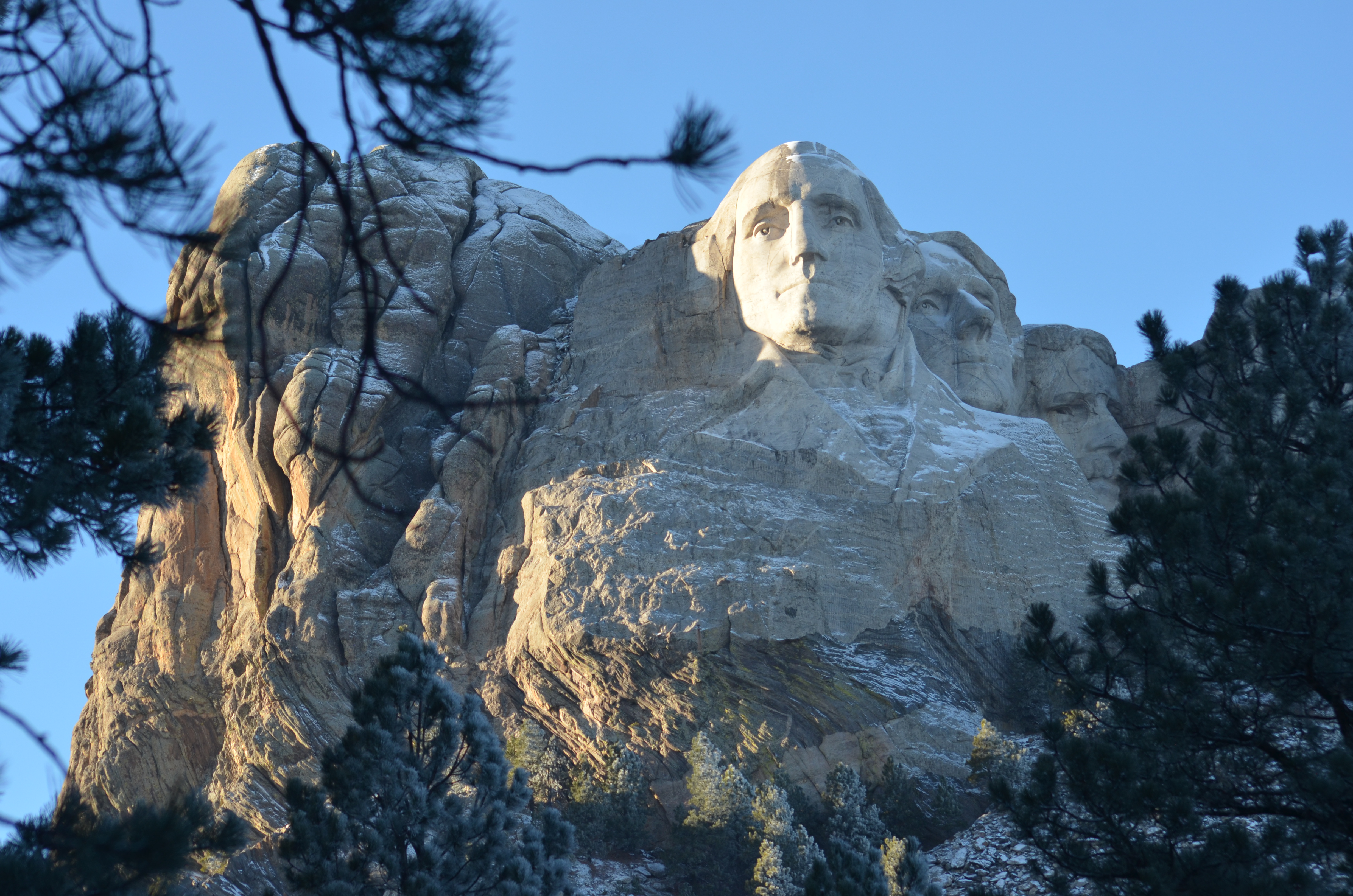 Mount Rushmore with snow on Washington's coat and head under a blue sky.