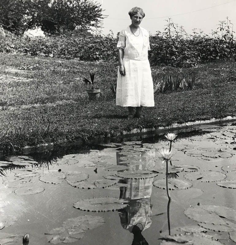 Helen Shaw standing by pond with lily pads and flowers