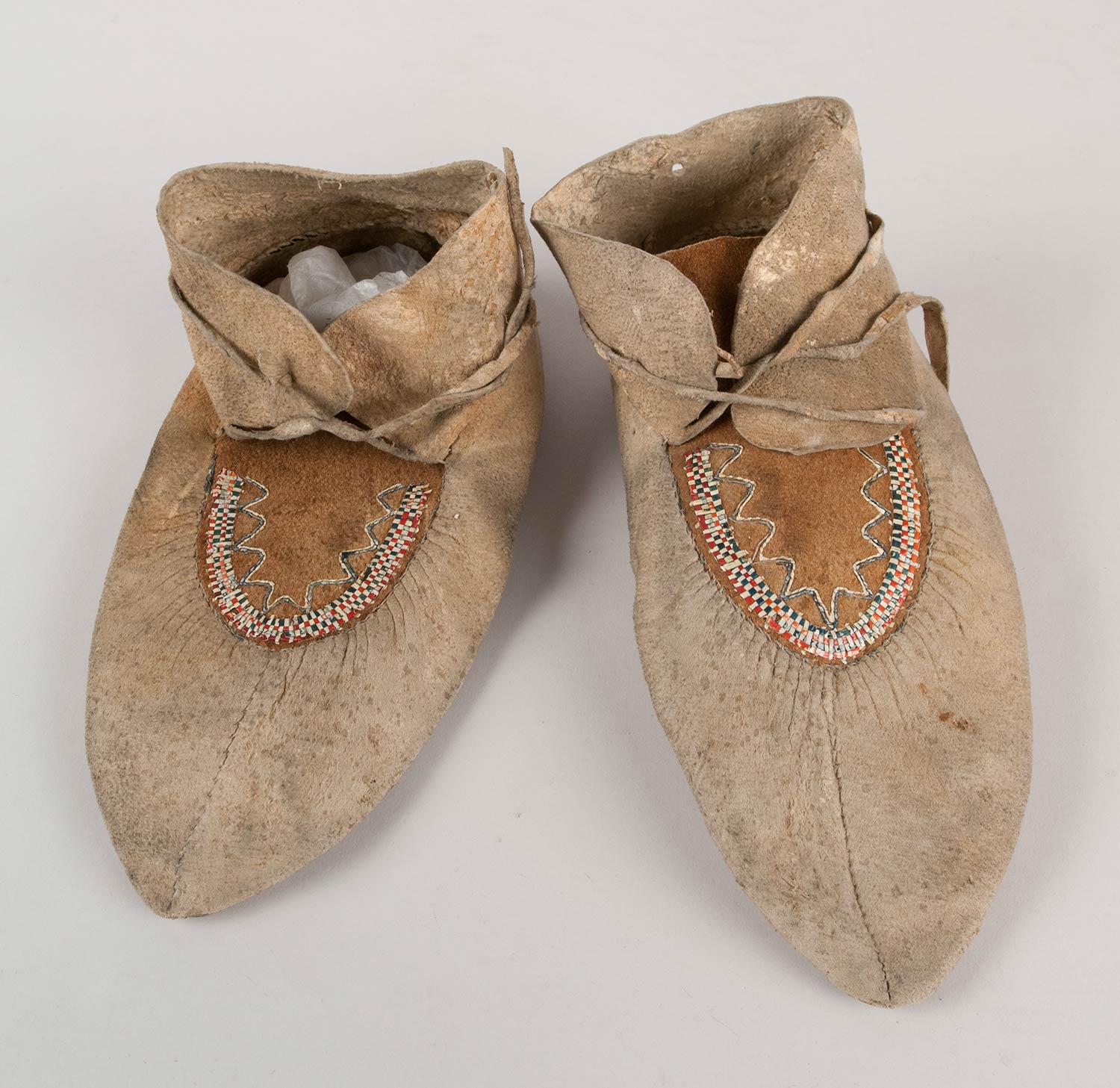 Pair of quillwork moccasins made from two pieces of hide, either caribou or moose. Quillwork design is a checkered weave of red, blue, and yellow quills.