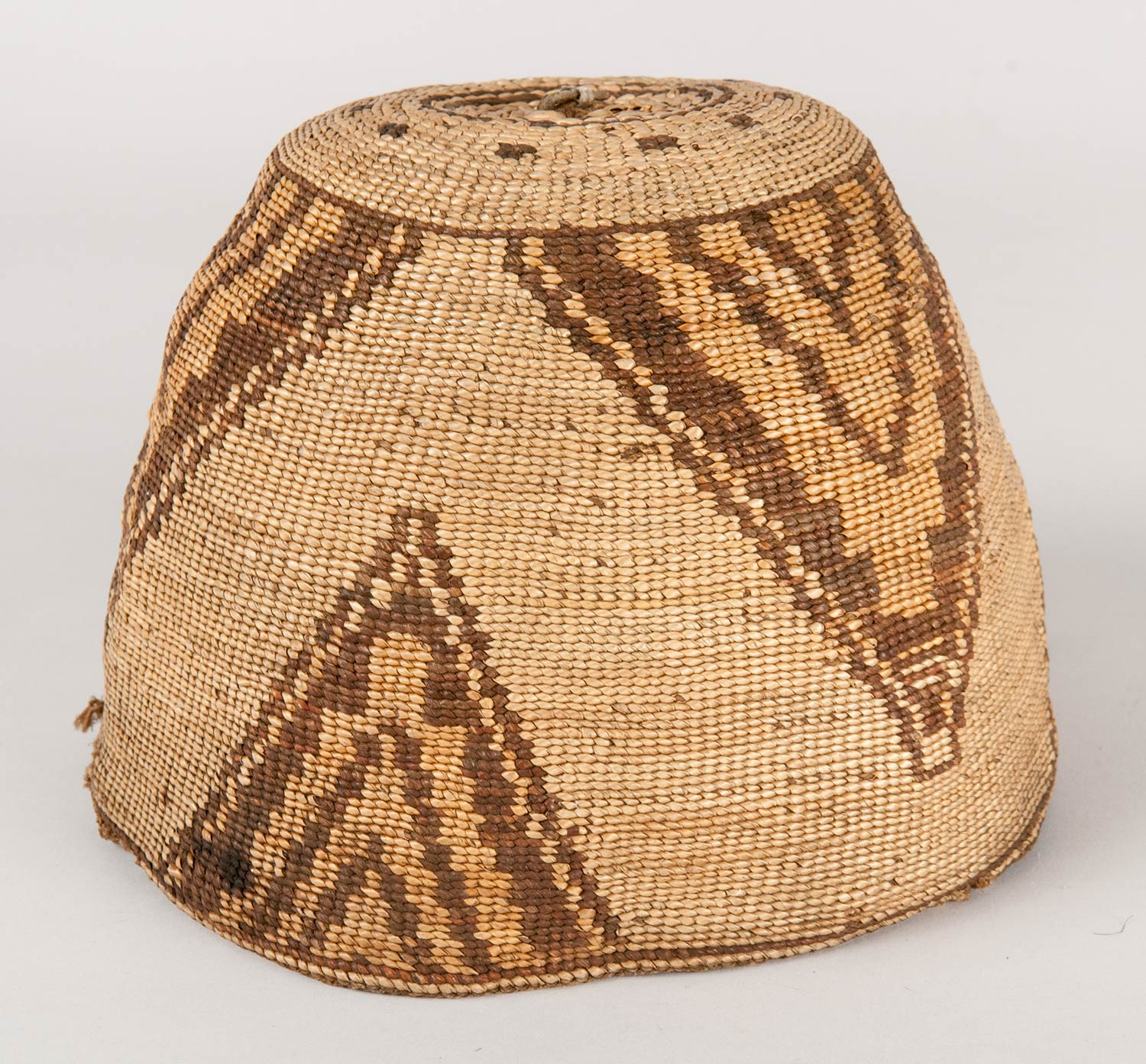 Subconical shaped basket hat made from hemp, beargrass, cedar root bark strips, and wool. Piece of cured hide located at top of hat, which was used to start the crown base.