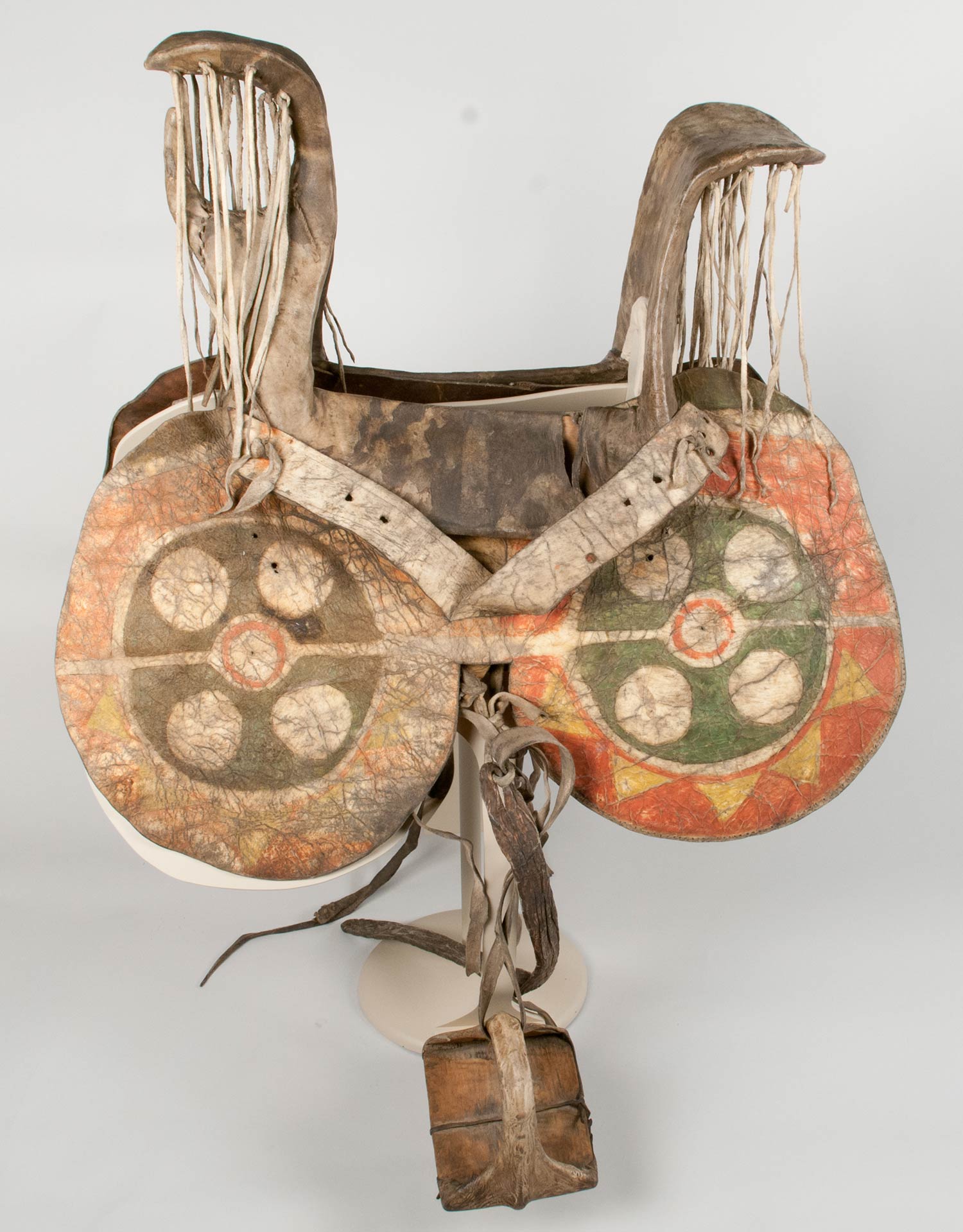 A woman's saddle made from a cottonwood frame with a rawhide covering. The rawhide saddle fenders features geometric designs of green, yellow, and red.