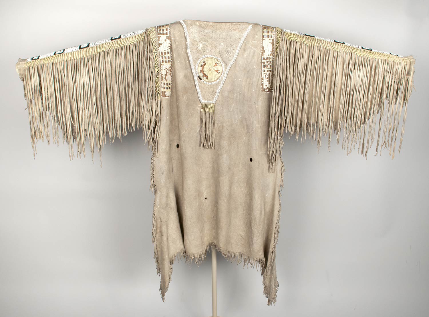Man's cured hide shirt decorated with quillwork, Venetian glass beads, wool cloth, and fringe. Body of the shirt is of the two-skin style with hair side outward and head section at top.