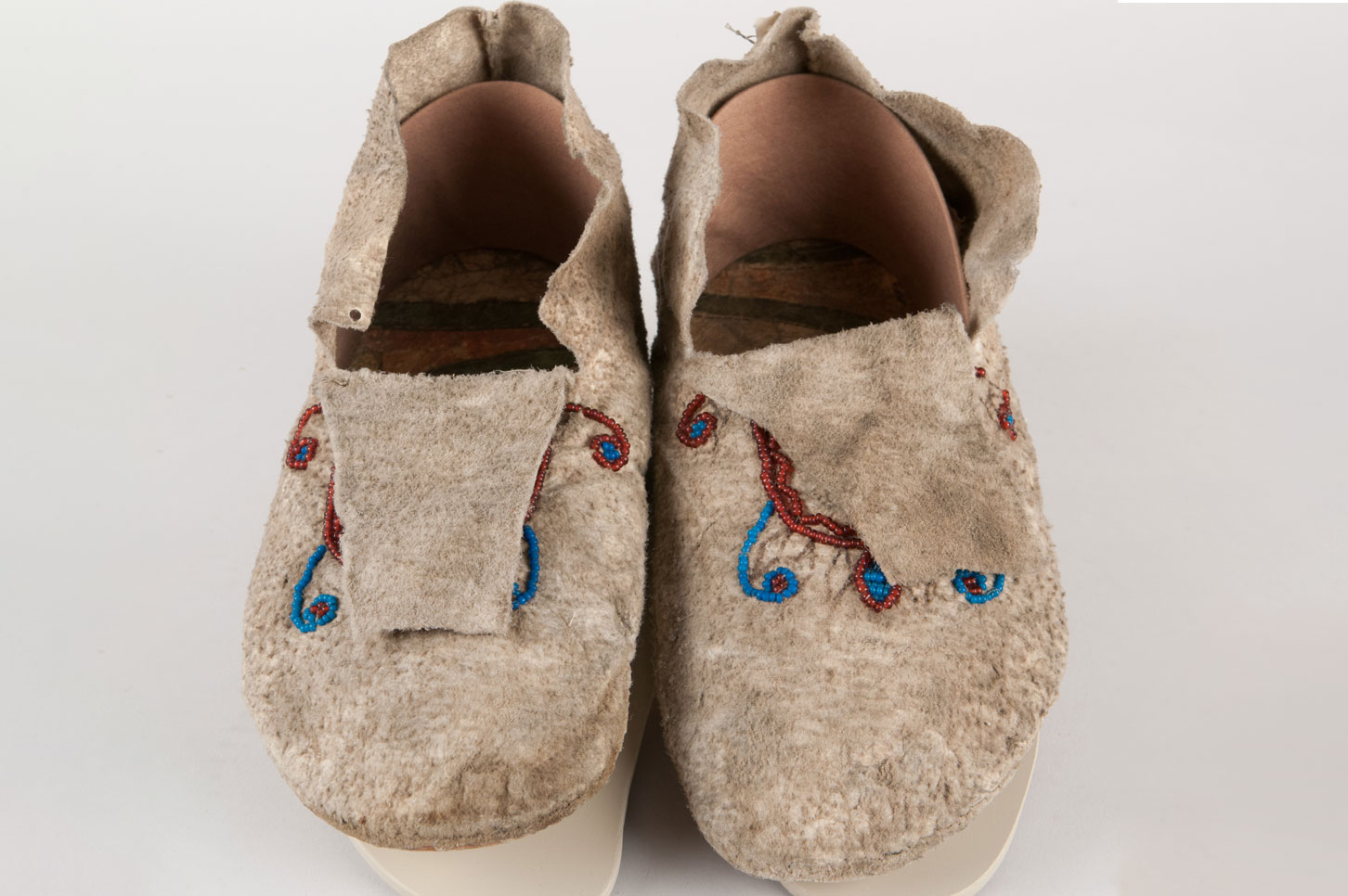 Two piece moccasins, constructed utilizing rawhide cut from a 'isaap'tekey or parfleche for the soles. The uppers being made made from deer hide, originally the summer hides or 'red hides' were favored for constructing moccasins, because the ticks on the deer were believed to make the hide more durable. 