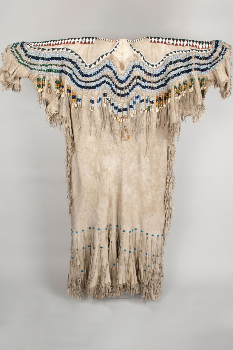 Woman's dress of two elk skins, decorated with glass beads, elk teeth, and fringe. The skins are large and left in natural form with hair left on legs and tail.