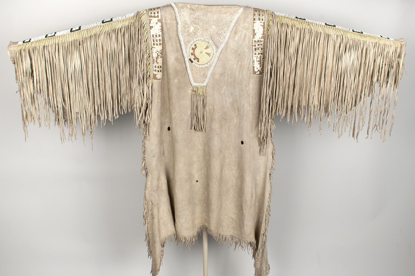 Man's cured hide shirt decorated with quillwork and black and white Venetian glass beads. Body of the shirt is of the two-skin style with hair side outward and head section at top.