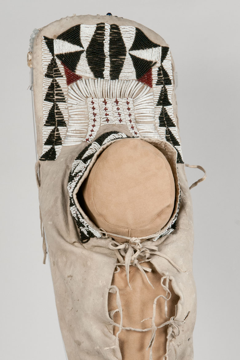 Teardrop shaped child's cradleboard made from a wooden board and covered with brain tanned deerskin. Decorated with  glass beads, dentalium shells, and elk teeth. 