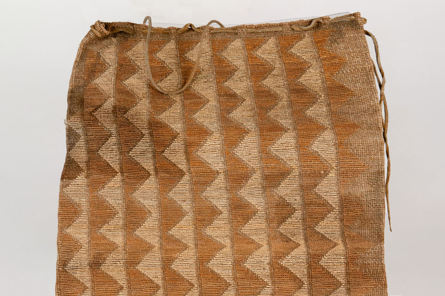 Large, flat cornhusk bag with a buckskin drawstring attached to the top of bag. Constructed using plain twining of Indian hemp with cornhusk false embroidery and dyed beargrass.