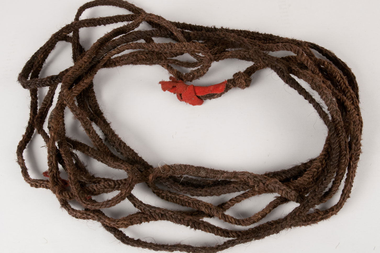 Woven bison hair rope with knotted ends decorated with red wool broadcloth. The weaving of the rope is done with five tightly woven two-ply twisted strands of lengths of bison hair approximately five-eight inches, which have been continuously added to each strand to produce length.