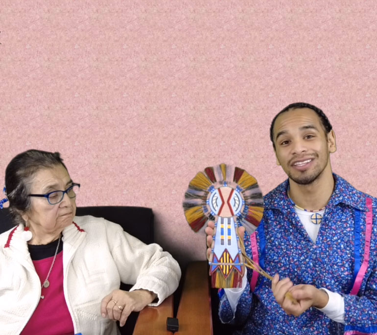 Native American woman sitting next to a Native American man. Native American man is holding a beaded piece of work he created.