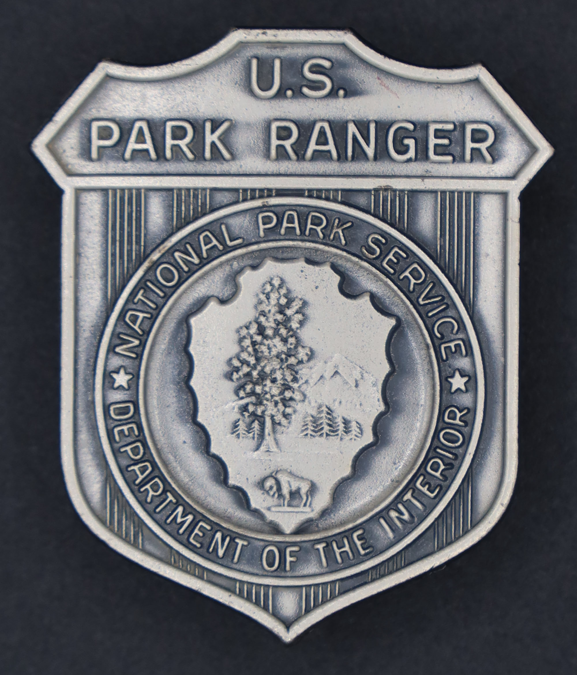 Silver shield-shaped badge marked U.S. Park Ranger. NPS arrowhead with National Park Service Department of the Interior encircling it in the middle.