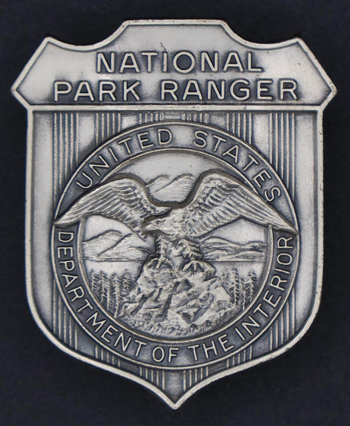 Silver shield-shaped badge marked National Park Ranger. The round seal in the middle has an eagle looking to its right.