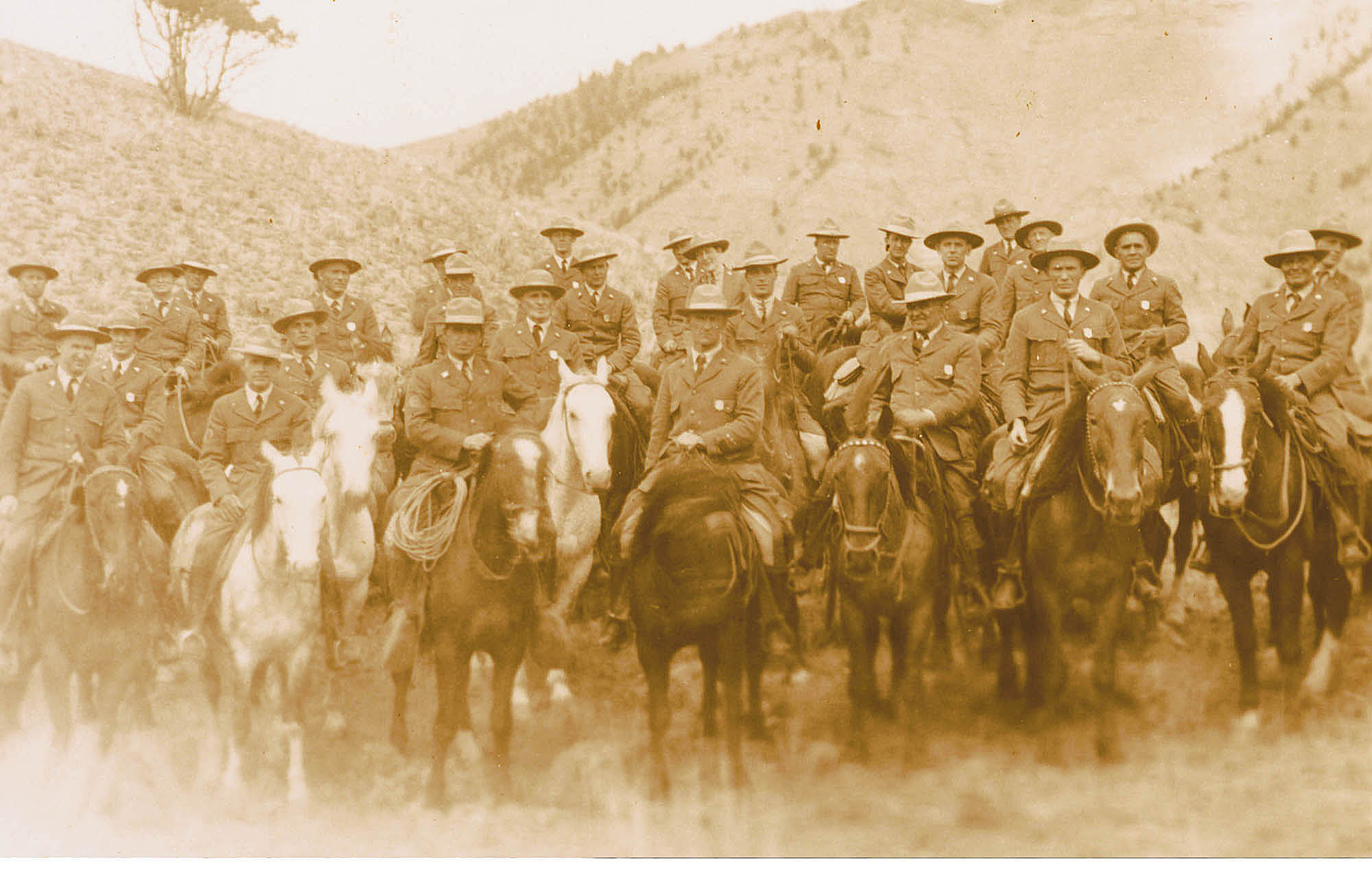 Twenty-seven men and one woman in NPS uniforms and broad brim hats pose on horses. Most wear shield-shaped badges.
