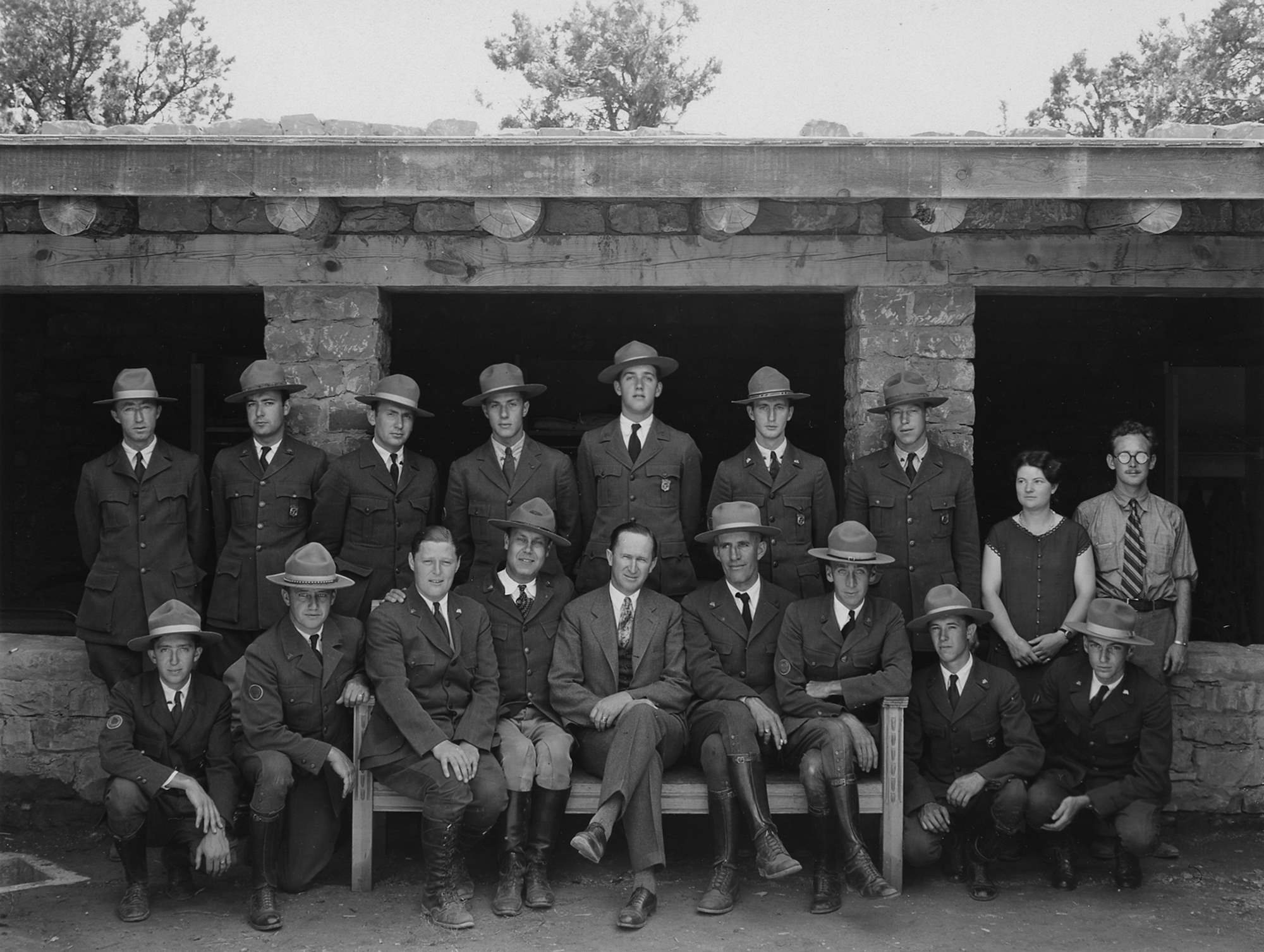 Seventeen men and a woman pose with Director Albright.  Shield shaped badges are on the jacket pockets of five uniformed rangers. 