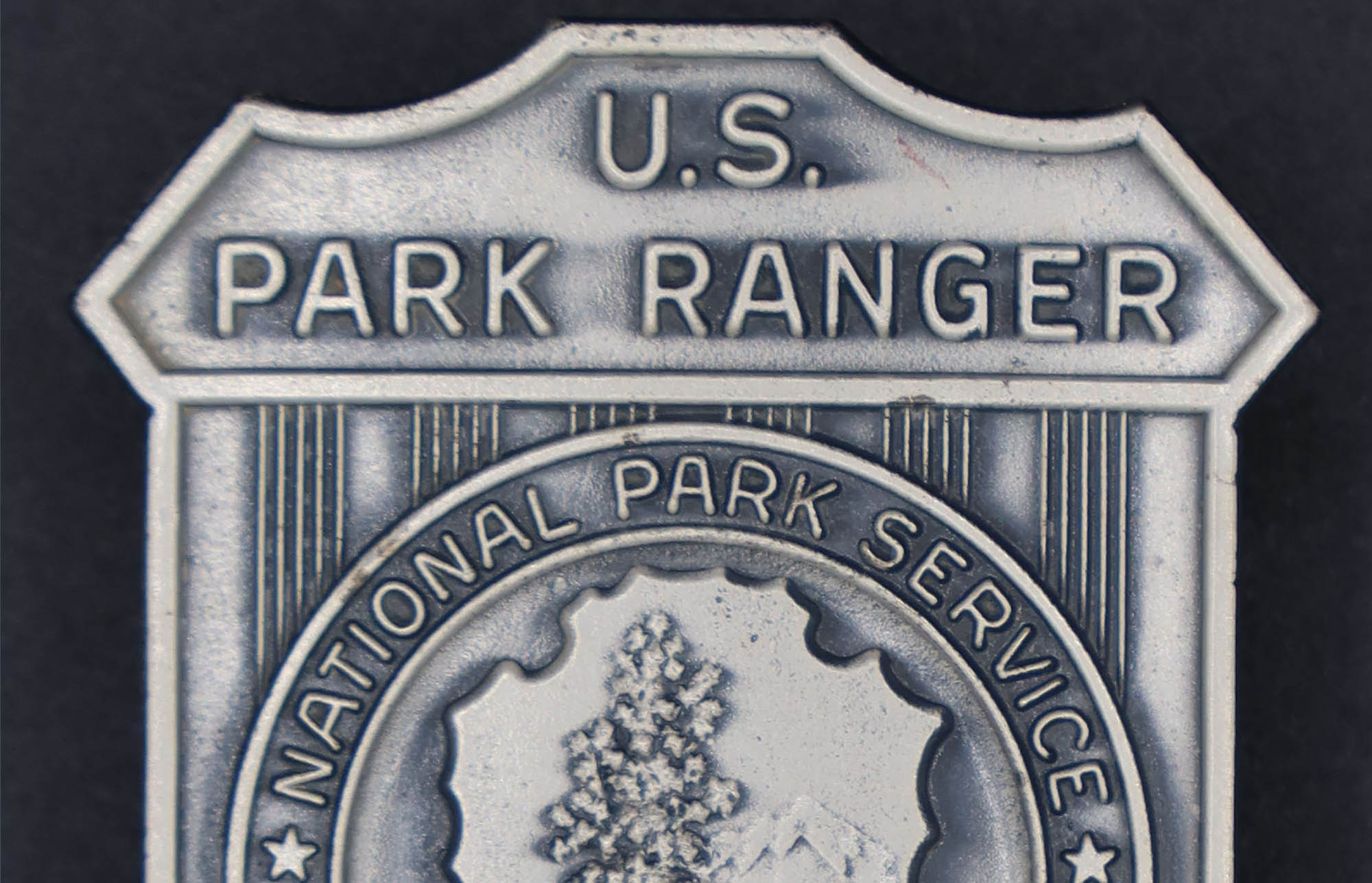 Silver shield-shaped badge marked U.S. Park Ranger. NPS arrowhead with National Park Service Department of the Interior encircling it in the middle.