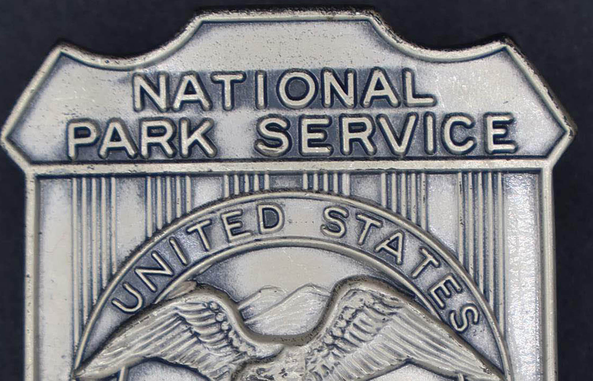Silver shield-shaped badge marked National Park Service. The round seal in the middle has an eagle looking to its right.