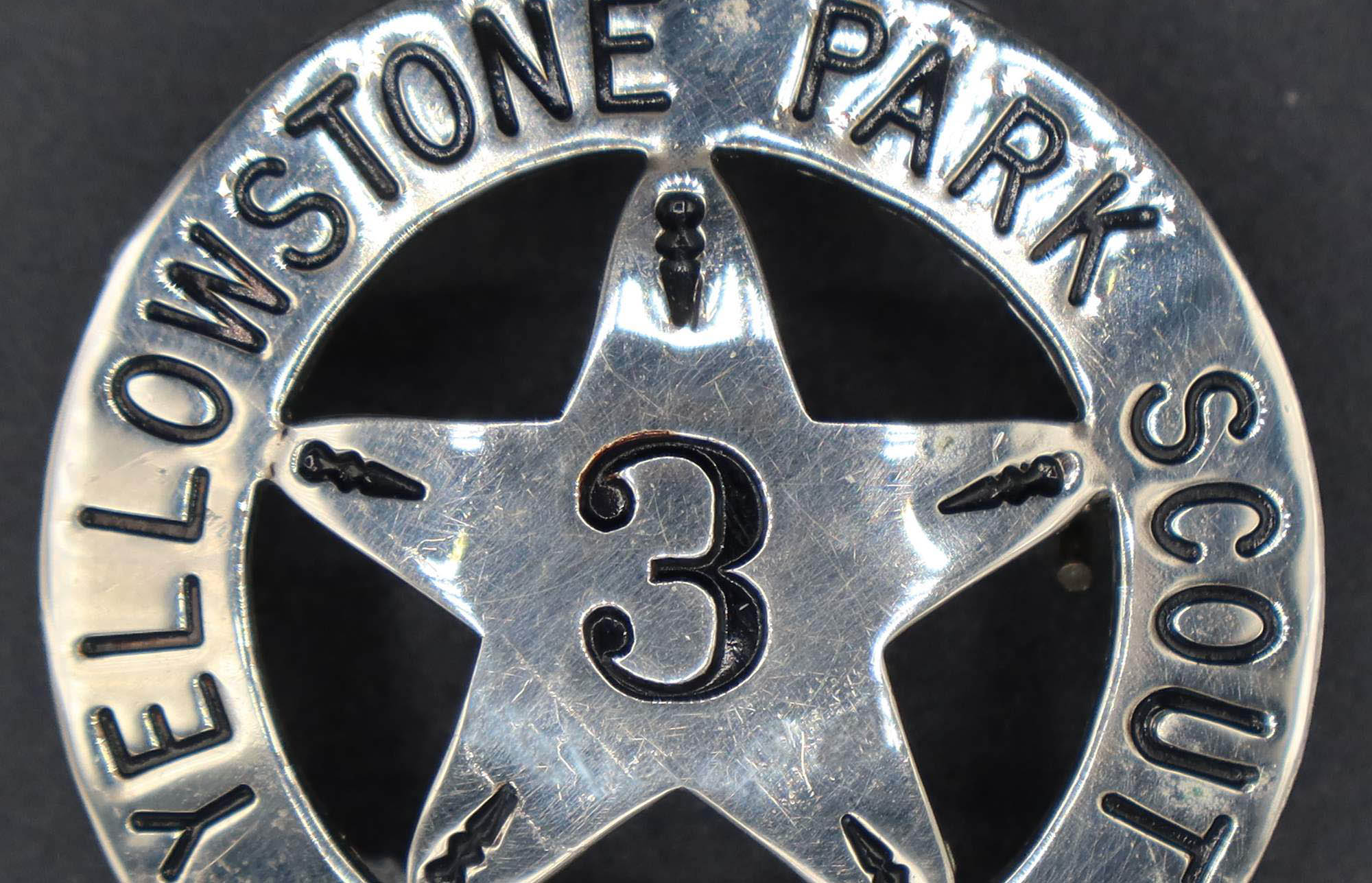Round silver badge with a central five-point star marked with the number 3. The rim is marked Yellowstone park scout.