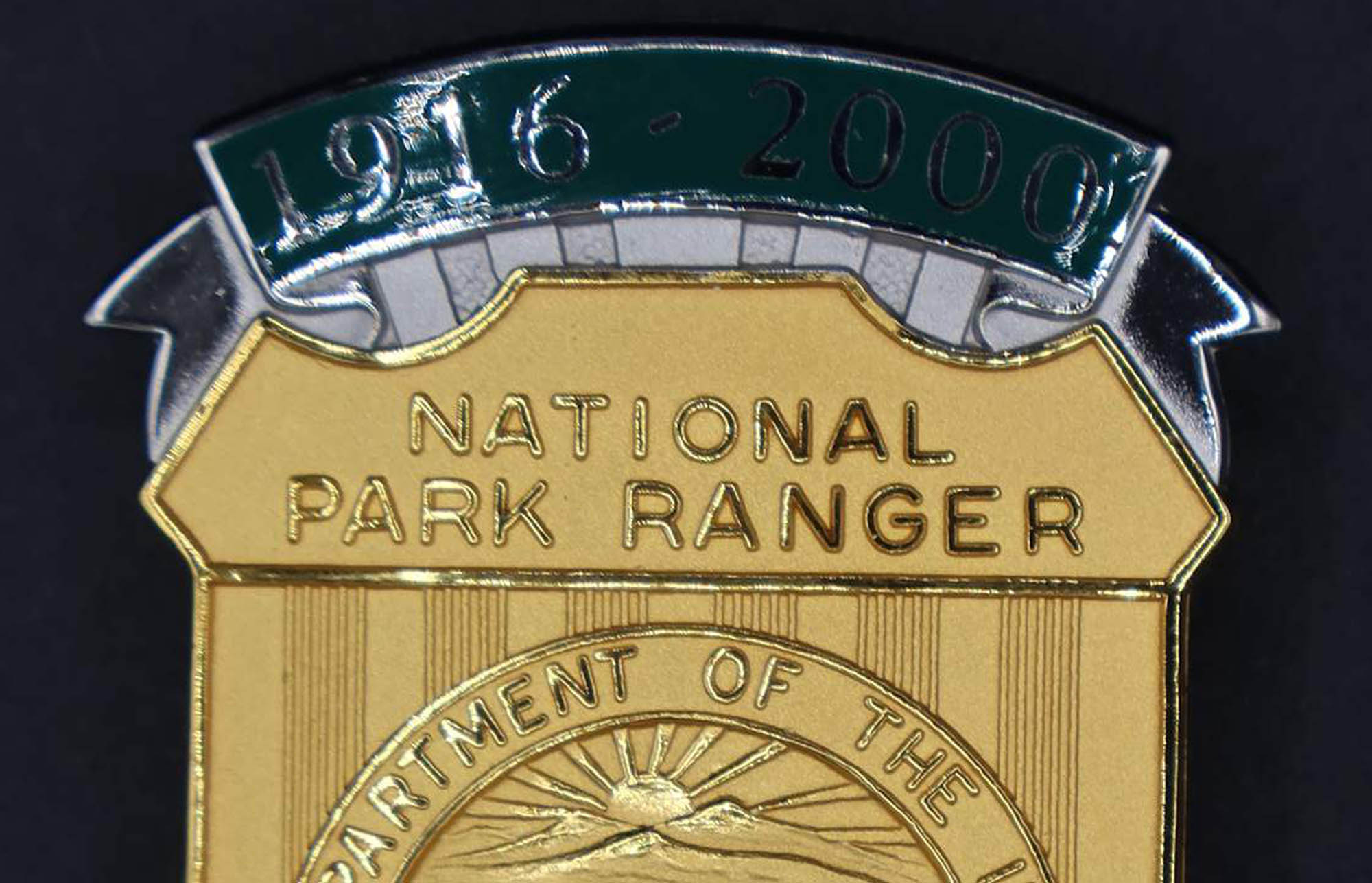 Gold shield-shaped bison badge marked National Park Ranger. Green banners at top and bottom read 1916-2000 and Preserving for Future Generations. 