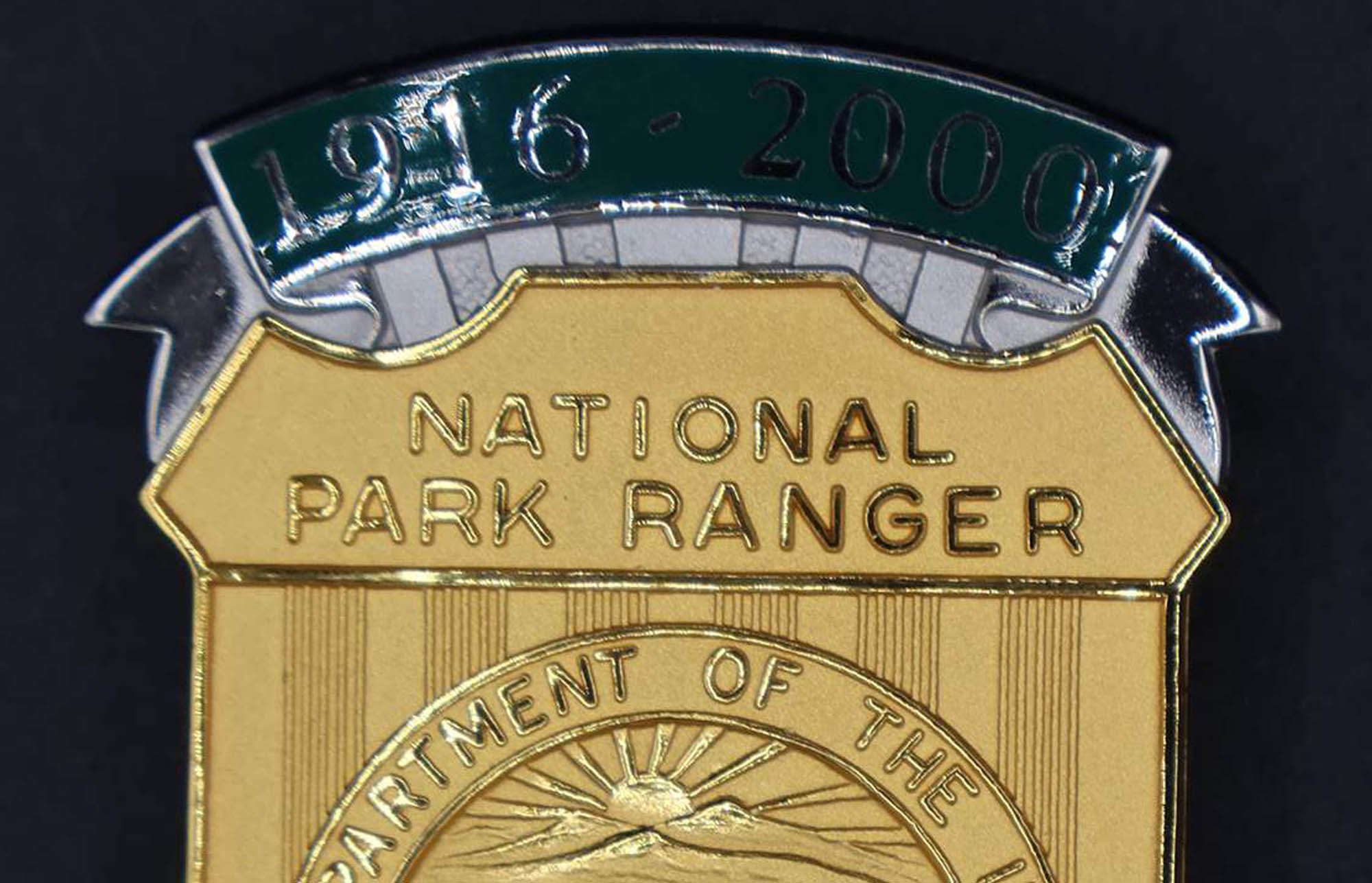 Gold shield-shaped bison badge marked National Park Ranger. Green banners at top and bottom read 1916-2000 and Preserving for Future Generations. 
